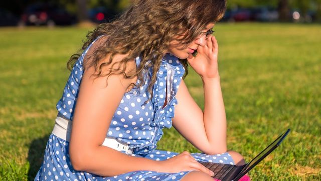 Joven encorvada con su computadora portátil en la falda