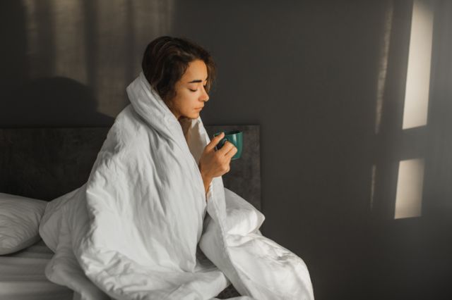 Una mujer enferma tiene fiebre y bebe té caliente en la cama y cubierta con una manta.