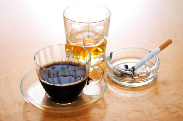 Taza de café, vaso con alcohol y un cigarrillo.