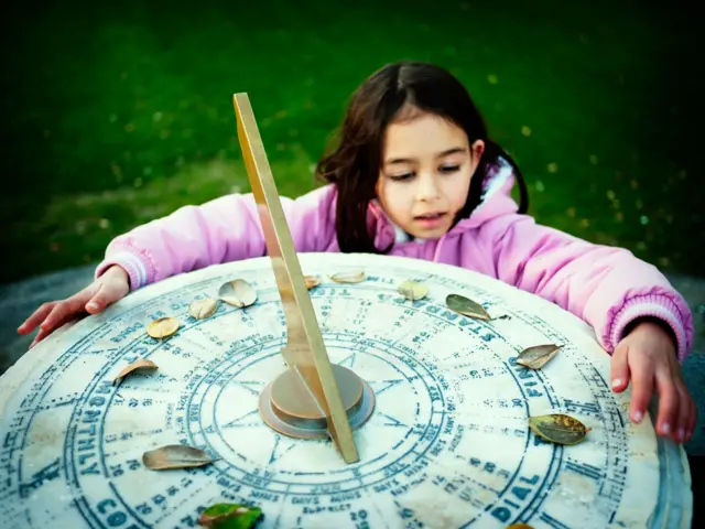 Niña al lado de un reloj de sol