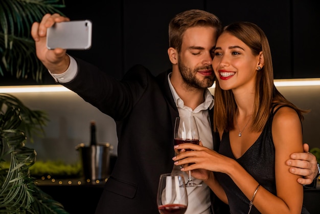 Pareja joven alegre tomando selfie mientras cena romántica en casa | Foto Premium